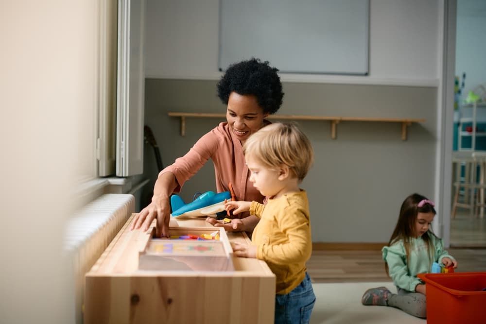 A dayhome caregiver helping a smiling toddler at an activity table